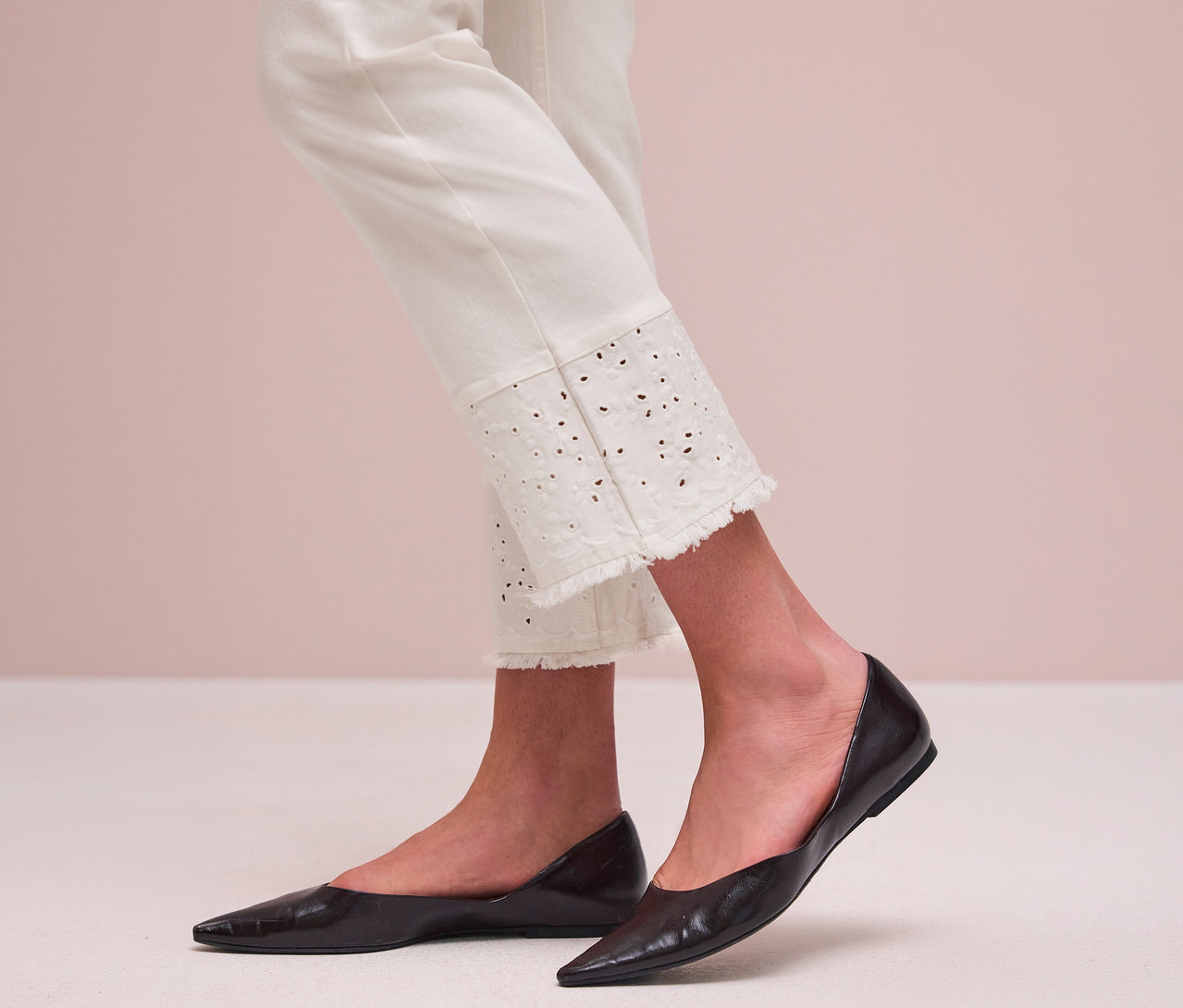 Personne portant un jean Street One blanc avec un ourlet brodé et effiloché et des ballerines noires à bout pointu.