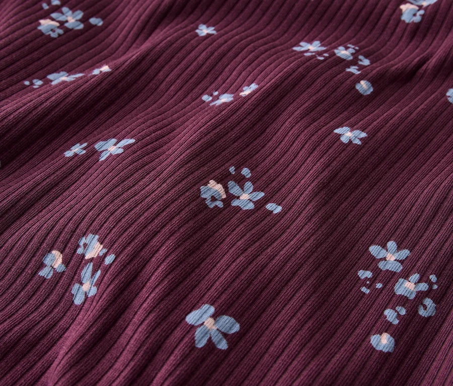 Gros plan d'un tissu côtelé bordeaux avec de petits motifs floraux bleu clair.