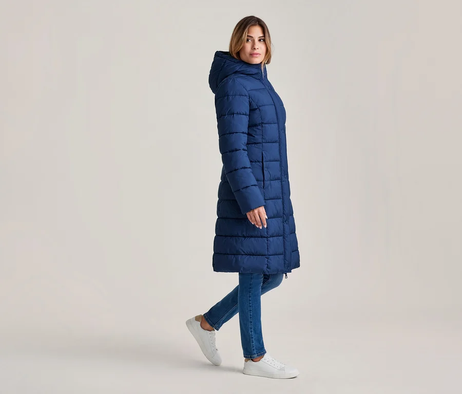 Femme marchant, vêtue d'un long manteau matelassé bleu marine à capuche, d'un jean bleu et de baskets blanches.