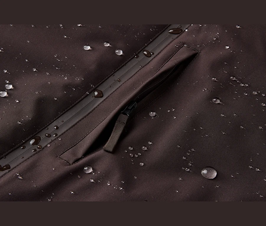 Gros plan sur un tissu imperméable marron foncé avec des gouttelettes d'eau et une poche zippée.