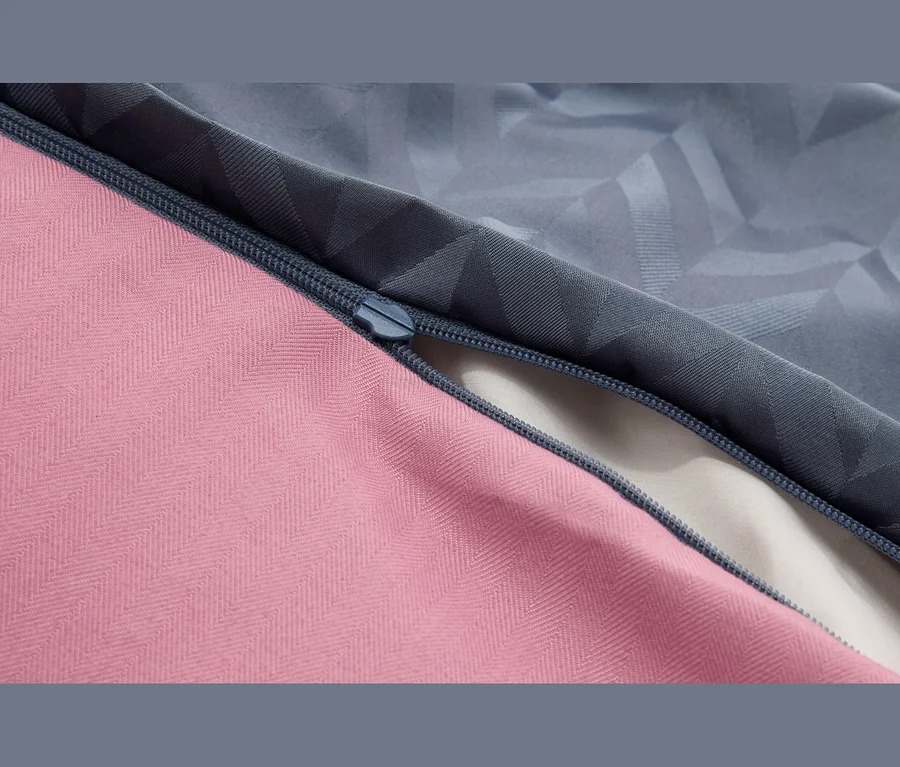 Gros plan d'une fermeture éclair bleu foncé reliant un tissu rose à chevrons et un tissu gris-bleu à motif géométrique, partiellement ouverte pour révéler un tissu clair en dessous.