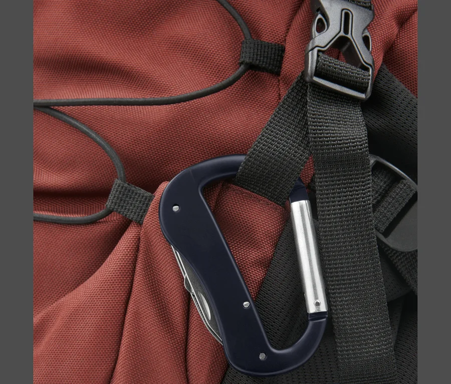 Gros plan d'un mousqueton avec un outil multifonction, fixé à un sac à dos rouge.