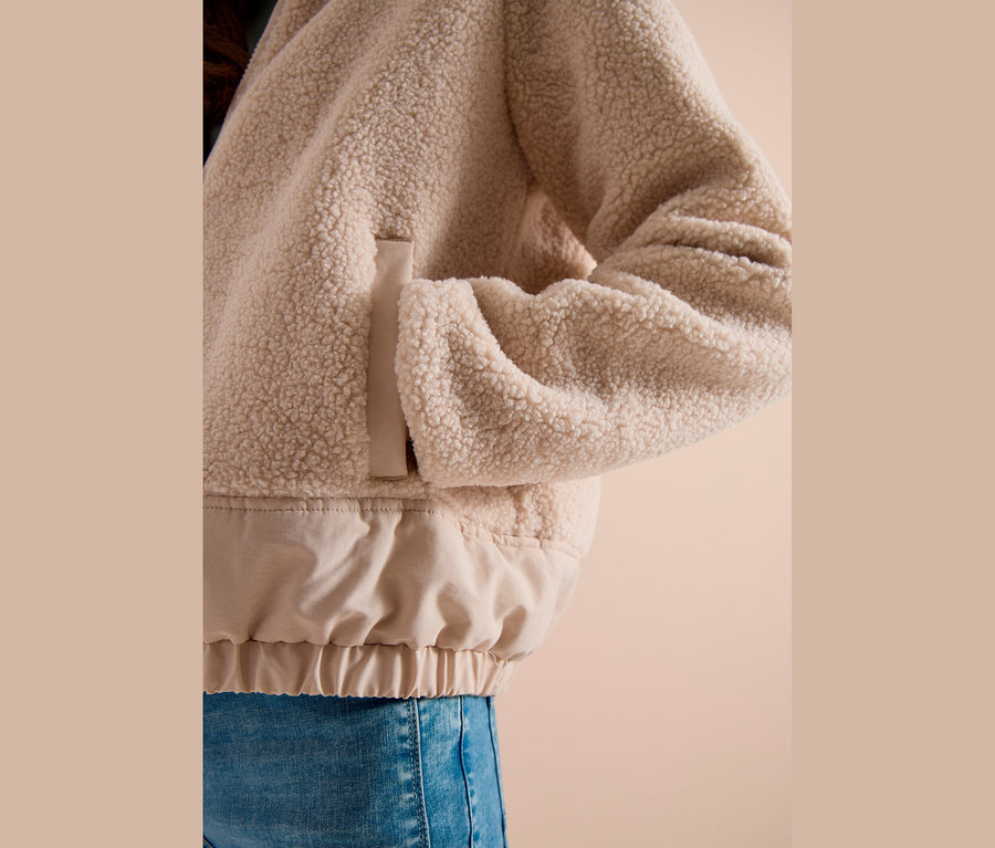 Personne portant une veste CECIL beige duveteuse avec un ourlet élastique lisse beige clair et un jean bleu, main dans la poche.