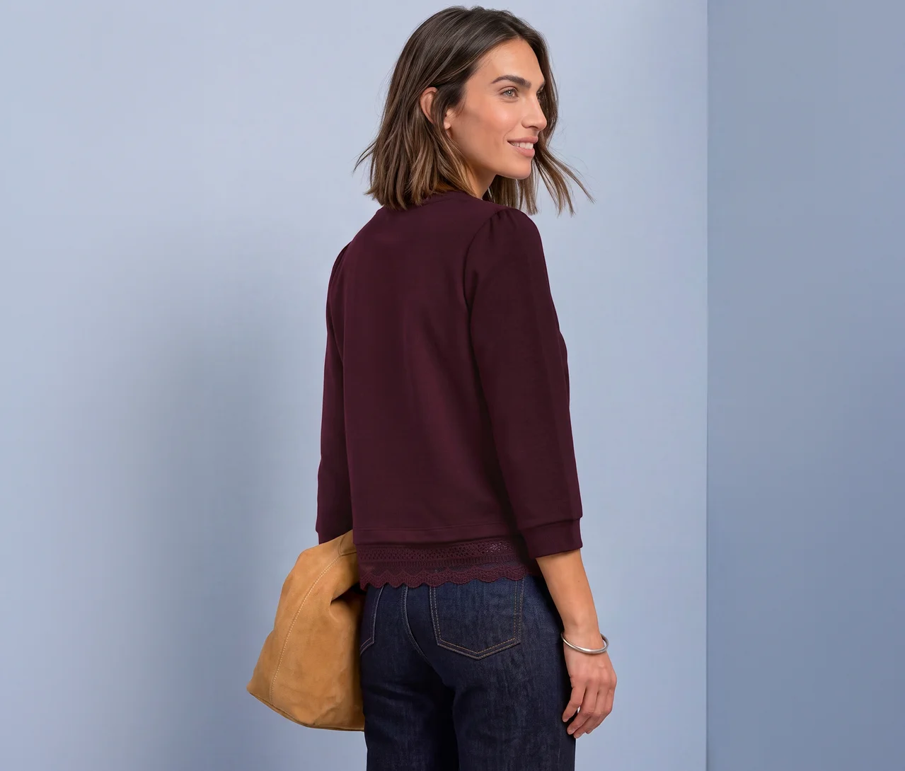 Femme portant un t-shirt en jersey 3/4 Street One rouge avec un ourlet en dentelle, un jean foncé et un sac beige, regardant par-dessus son épaule.