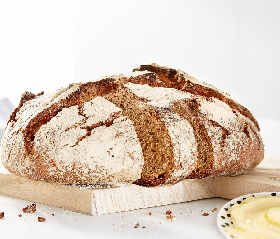 Une miche de pain sur une planche à découper en bois à côté d'une assiette de beurre.
