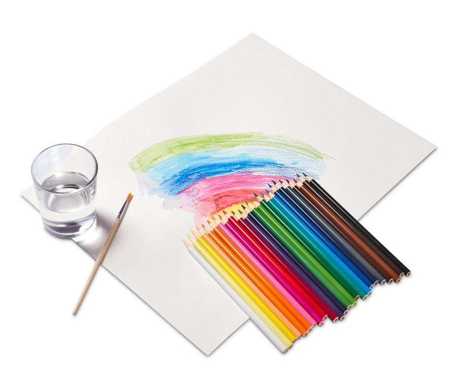 Des crayons de couleur aquarelle et un pinceau sont posés sur du papier à côté d'un verre d'eau.