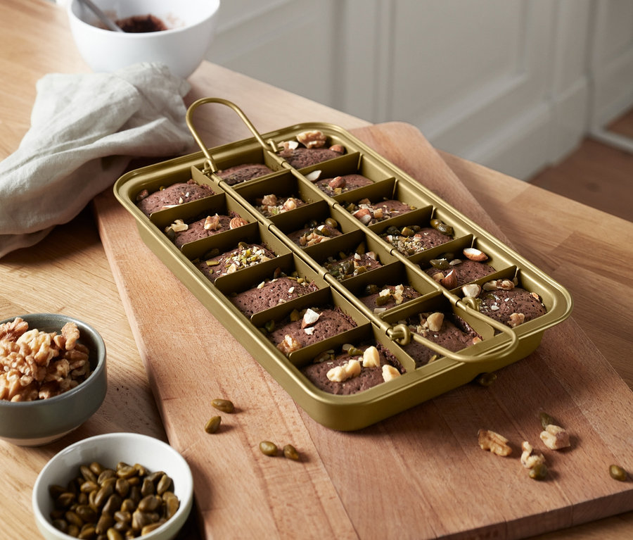 Un moule à brownie doré avec poignée rempli de petits brownies sur une planche à découper.