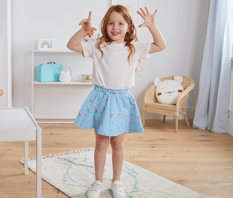 Une fille pose dans une chambre d'enfant et porte une jupe en jersey avec un short en coton bio.