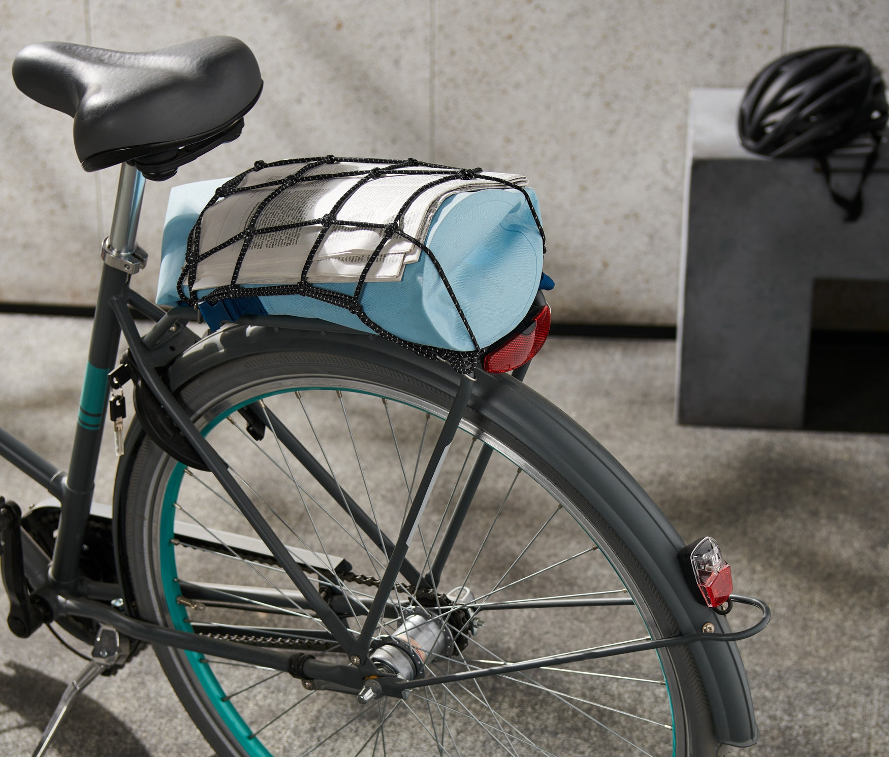 Sur un vélo, un filet pour porte-bagages de vélo maintient un sac bleu et un journal.