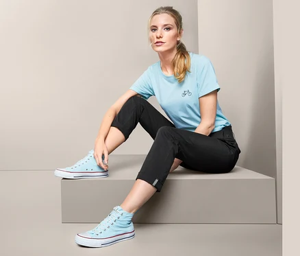 Une femme est assise sur une marche et porte un pantalon fonctionnel, un t-shirt bleu et des baskets bleues.