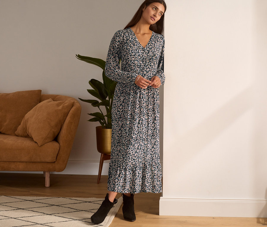 Une femme appuyée contre un mur porte une robe maxi à fleurs et des bottines noires.