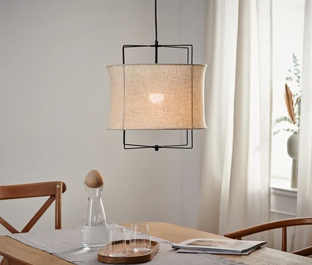Une suspension avec abat-jour textile est suspendue au-dessus d'une table en bois.