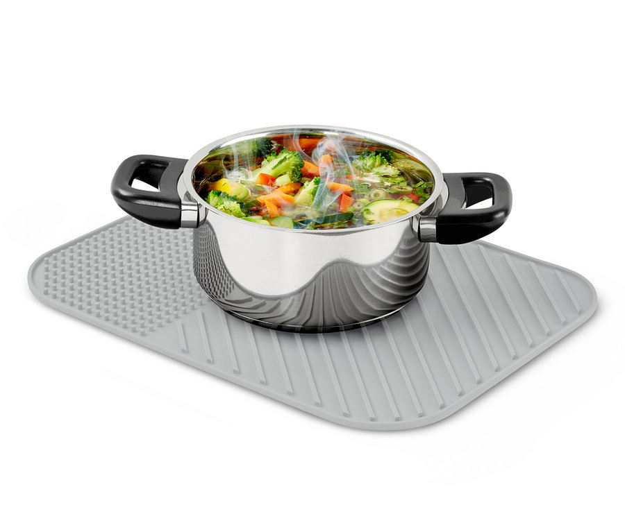 Une casserole en acier inoxydable remplie de légumes cuits repose sur un tapis égouttoir à vaisselle en silicone gris.