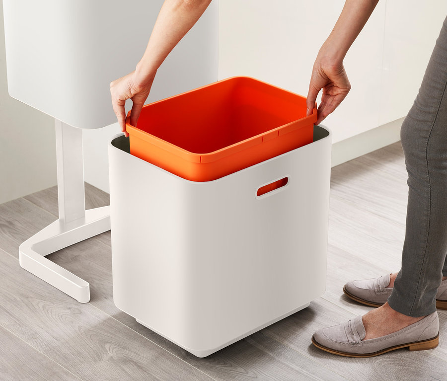 Une femme place un récipient orange dans une poubelle de tri sélectif Joseph Joseph.