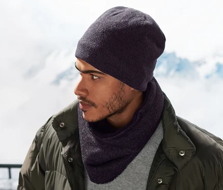 Homme portant une écharpe-tube en maille polaire bleue et un bonnet, avec des montagnes enneigées en arrière-plan.