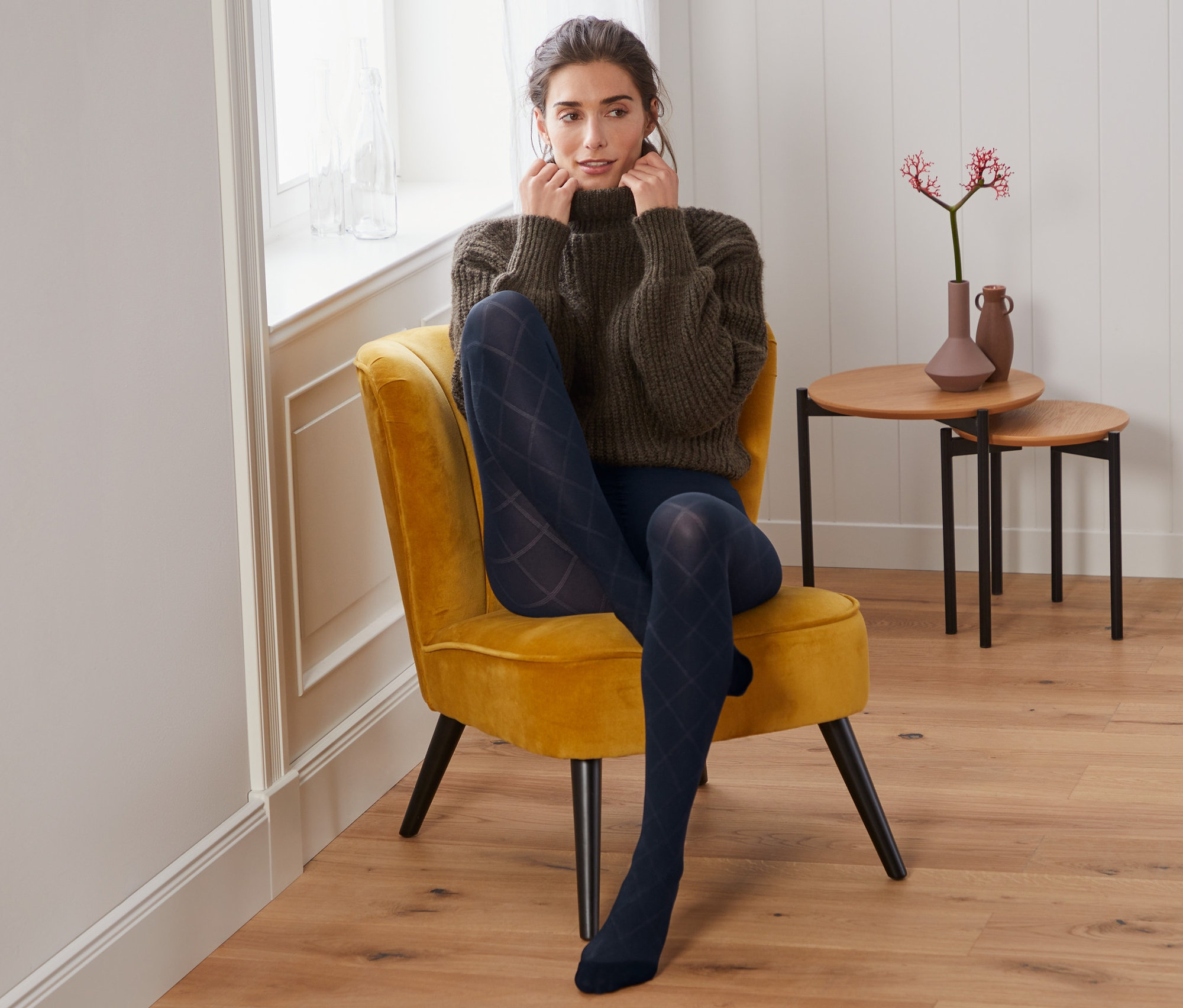 Une femme est assise dans un fauteuil et porte des collants fins avec une structure à carreaux.
