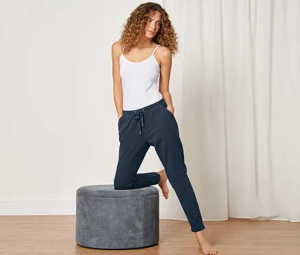 Femme posant en pantalon d’intérieur bleu foncé et débardeur blanc, une jambe sur un tabouret gris.