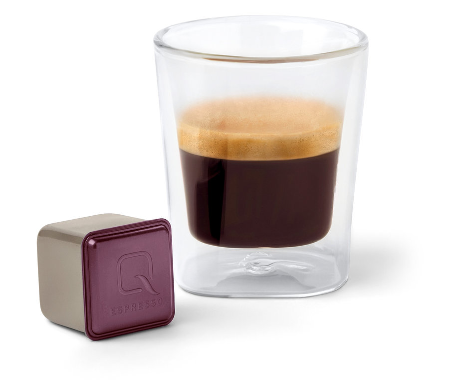 Une capsule Qbo Espresso ORO TOLIMA à côté d'une tasse à expresso.