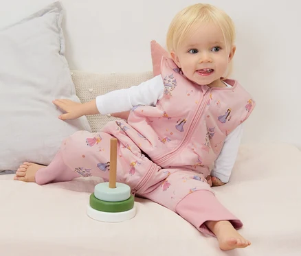 Un bébé est assis sur un matelas et porte une gigoteuse avec jambes, 2,5 TOG, env. 90 cm.