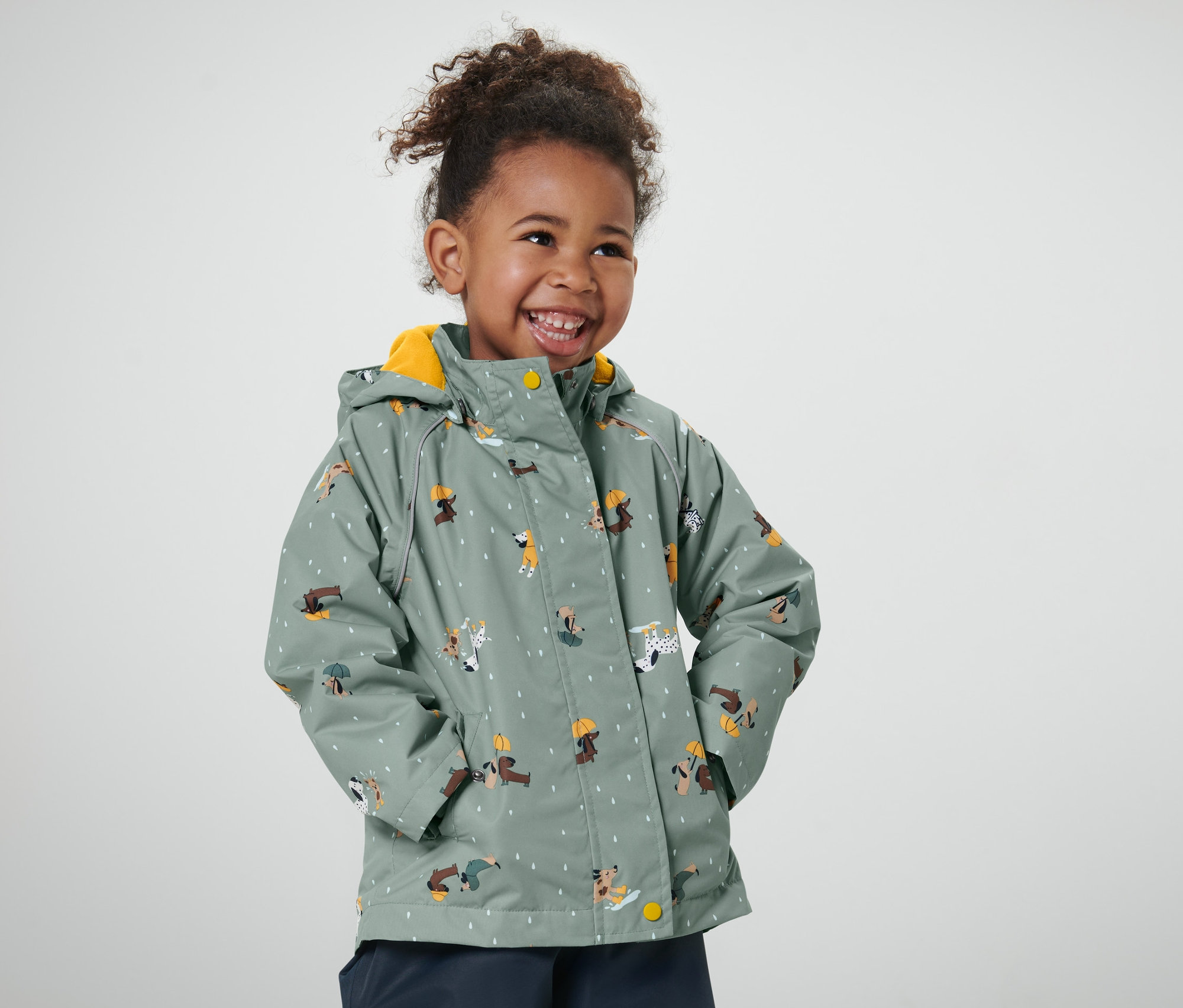 Fillette souriante portant une veste de pluie thermique pour enfant avec motif de chiens.