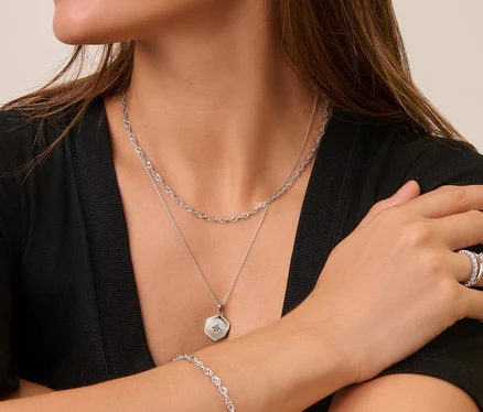 Une femme portant des bijoux en argent : des puces d’oreille avec arc en zircons en argent 925, une chaîne en argent 925 Singapour, une chaîne en argent 925 hexagone, une anneau en argent 925 solitaire, une bracelet en argent 925 Singapour et une anneau argent 925 mémoire.