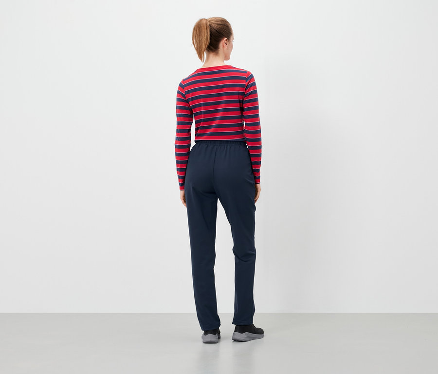 Vue de dos d'une femme aux cheveux bruns attachés en queue de cheval, portant un t-shirt à manches longues rayé rouge et bleu et un pantalon bleu foncé.