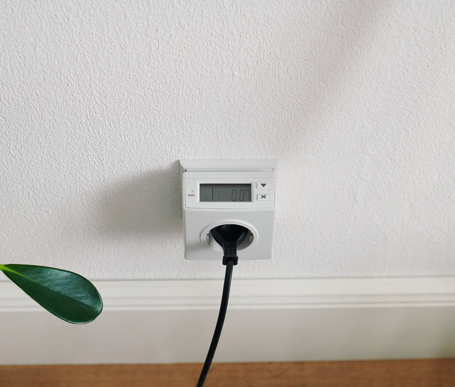 Appareil de mesure de la consommation d'énergie blanc branché sur une prise blanche sur un mur blanc avec un câble noir.