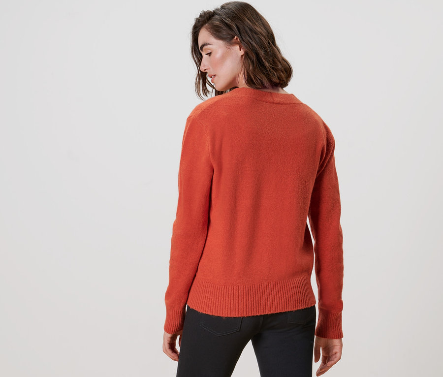 Vue arrière d'une femme portant un cardigan orange à encolure en V et un pantalon noir.
