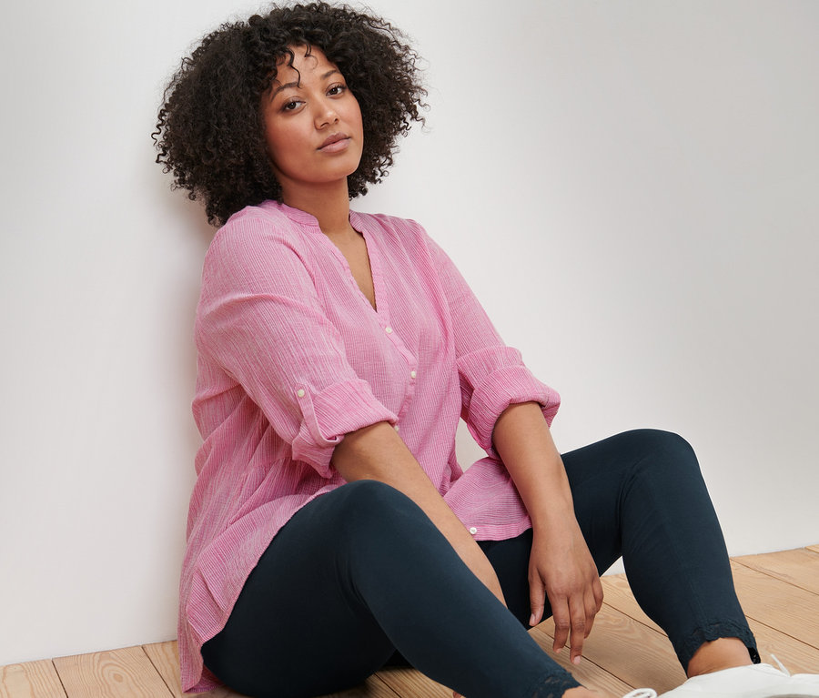 Une femme est assise par terre et porte une tunique longue rayée et un legging avec bord en dentelle.