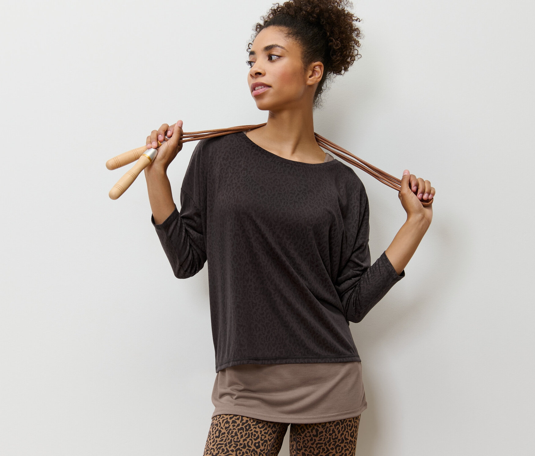 Femme posant avec un t-shirt de sport 2 en 1 marron et une corde à sauter.