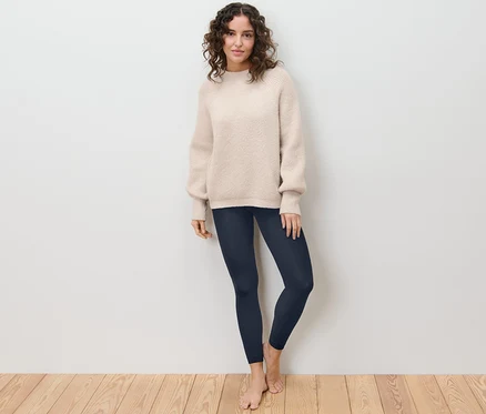 Une femme debout, pieds nus, portant un legging thermique et un pull.