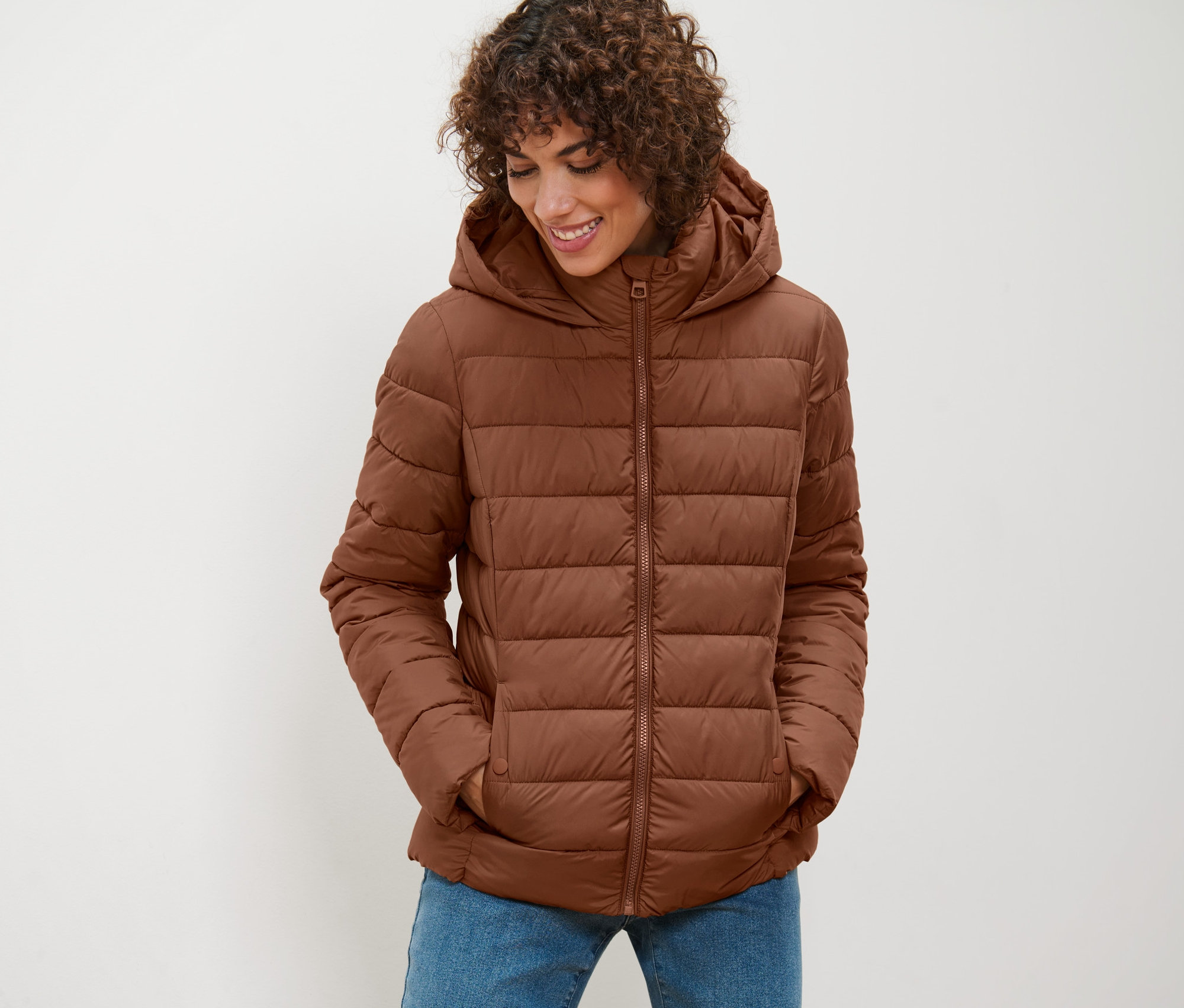 Une femme portant une veste matelassée à capuche cognac regarde vers le bas.