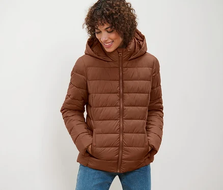 Une femme portant une veste matelassée à capuche cognac regarde vers le bas.