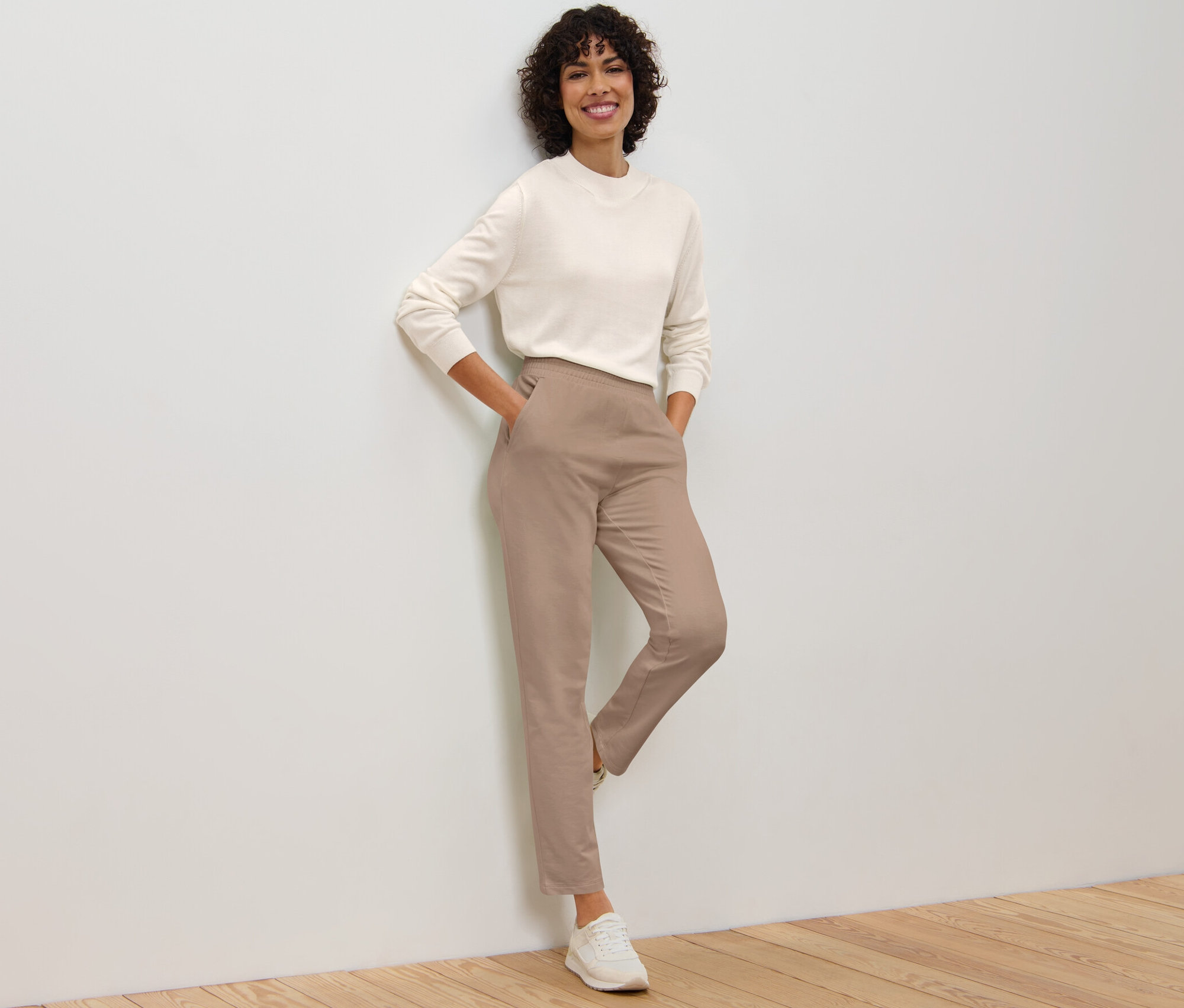 Femme appuyée contre un mur posant en pantalon de jogging beige.