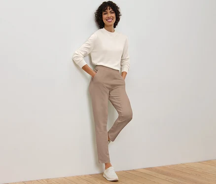 Femme appuyée contre un mur posant en pantalon de jogging beige.