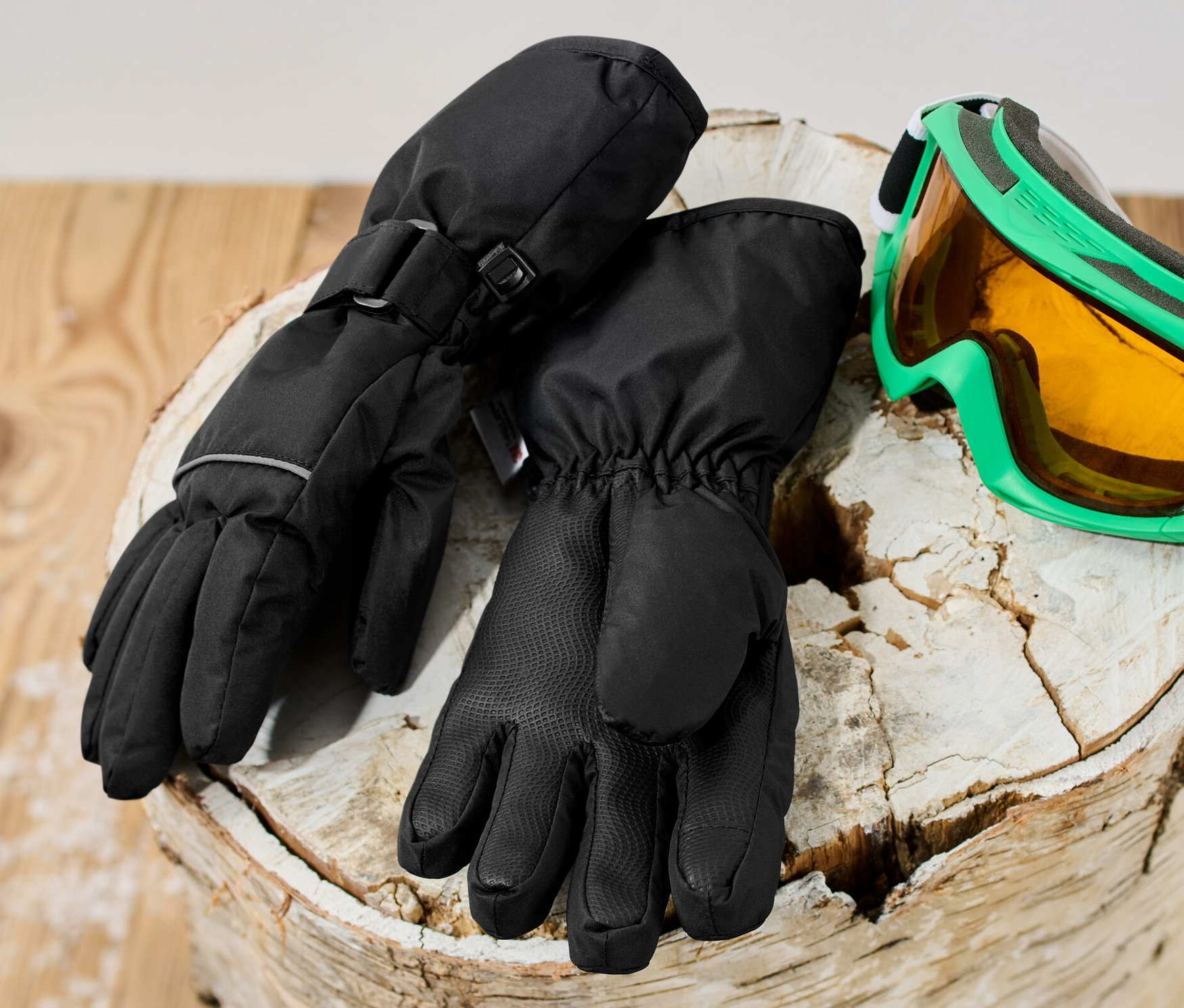 Des gants d’hiver de ski pour enfant noirs sont posés sur une bûche à côté d'un masque de ski.