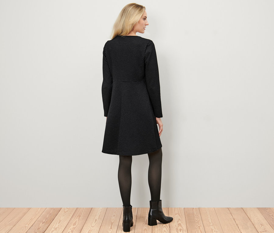 Une femme blonde, vue de dos, porte une robe en jacquard scintillant, des collants noirs et des bottes.