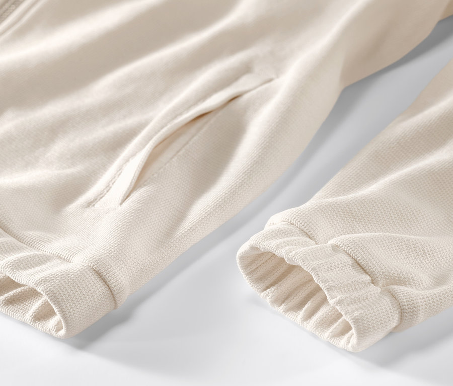 Gros plan sur une jaquette en sweat blanc crème avec fermeture éclair et poche.