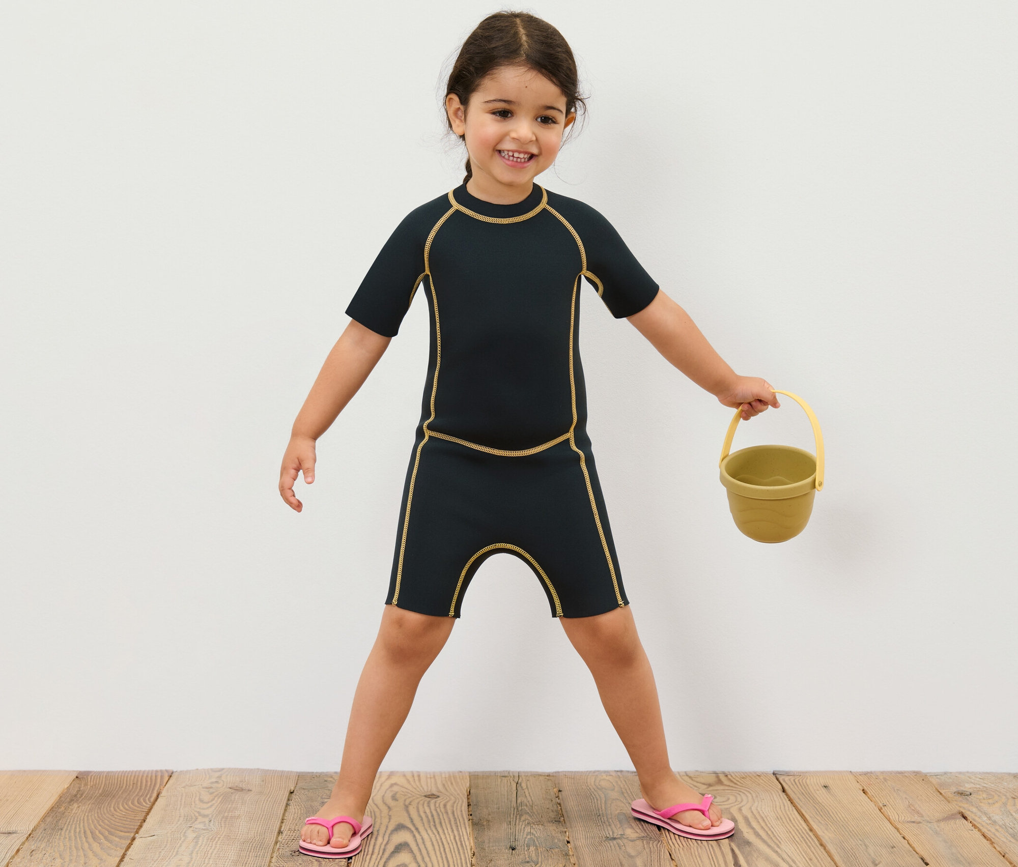 Fillette en costume en néoprène pour enfant tenant un seau jaune.