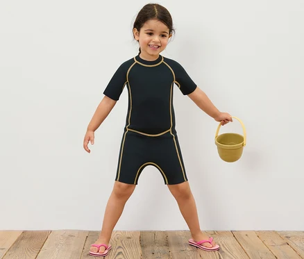 Fillette en costume en néoprène pour enfant tenant un seau jaune.