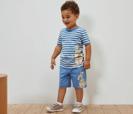 Un garçon debout porte 2 t-shirts pour enfant avec application et un short avec un motif de kangourou.