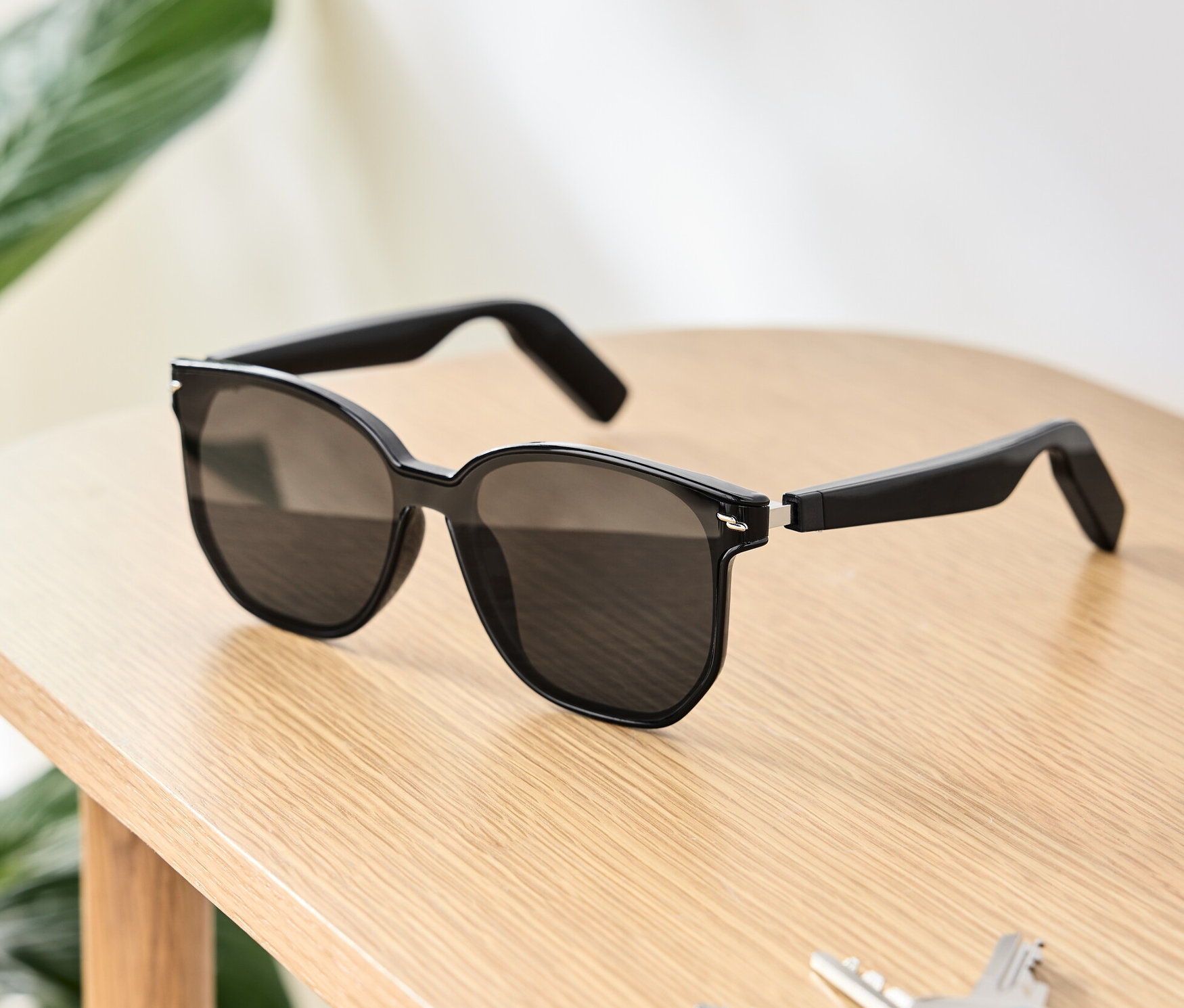Des lunettes de soleil noires avec écouteurs Bluetooth® sont posées sur une table en bois à côté de clés et d'un portefeuille.