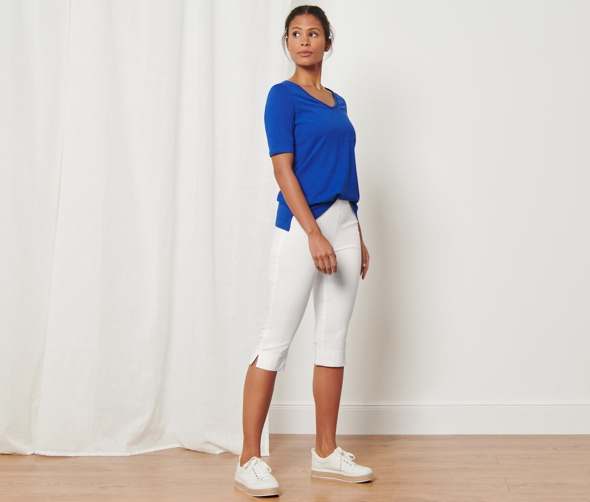 Femme debout en corsaire stretch blanc et t-shirt bleu.