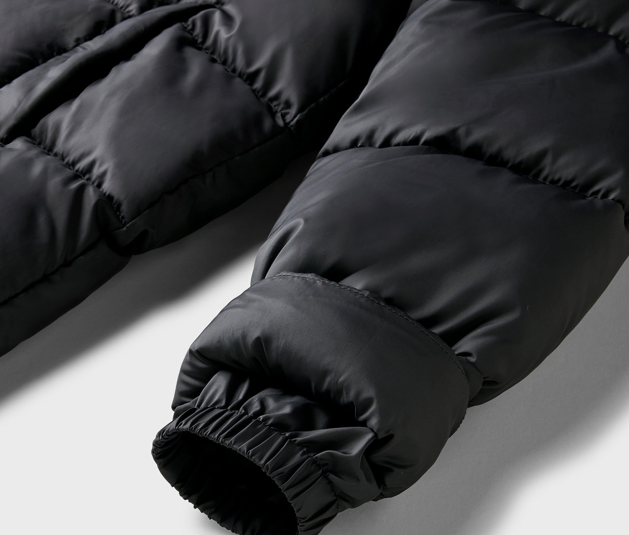Gros plan sur la manche d'un manteau matelassé noir avec poignet élastique.