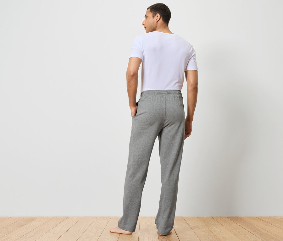 Un homme vu de dos porte un pantalon de survêtement gris et un t-shirt blanc.