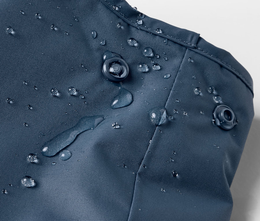 Gros plan sur un pantalon de pluie thermique bleu pour enfant avec des gouttes d'eau et des boutons-pression.