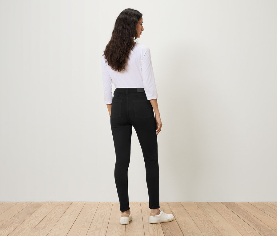 Une femme se tient dos à l'appareil photo, portant un jean noir et une chemise blanche.