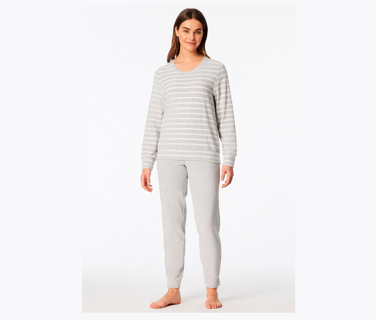 Une femme se tient debout, pieds nus, portant un pyjama gris rayé blanc.