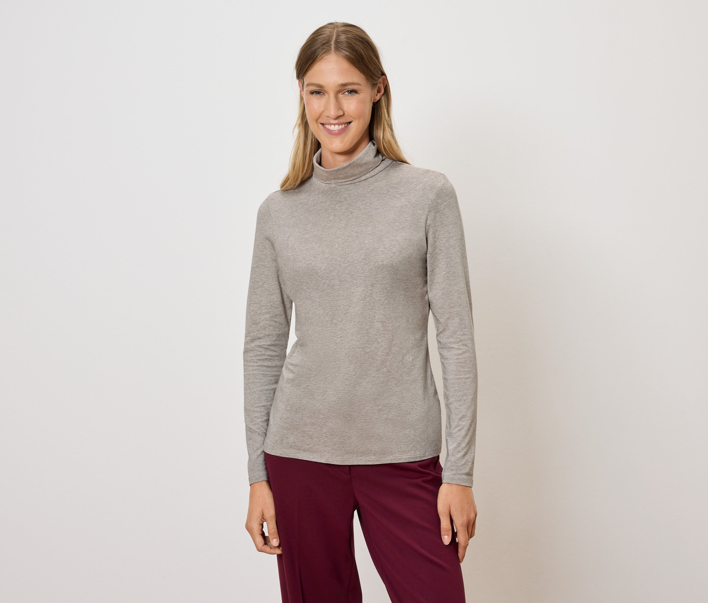 Femme posant dans un pull à col roulé gris et un pantalon bordeaux.
