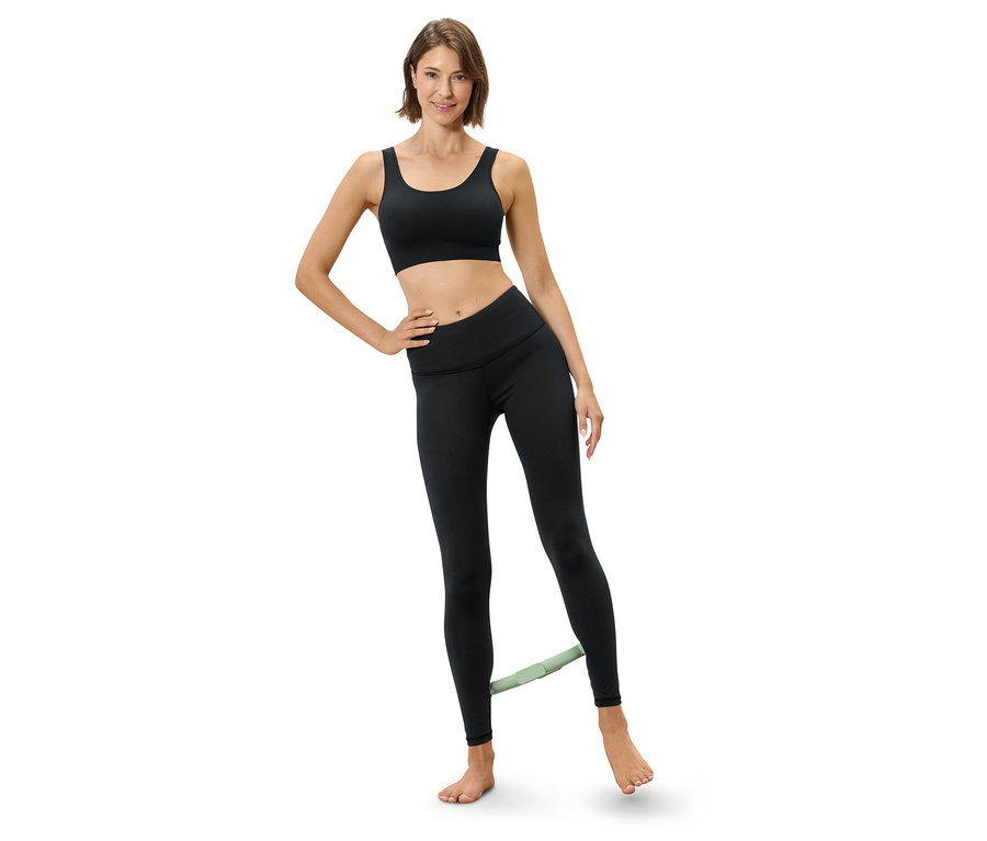 Femme faisant de l'exercice avec une bande de résistance autour des jambes, vêtue d'une brassière de sport et de leggings.